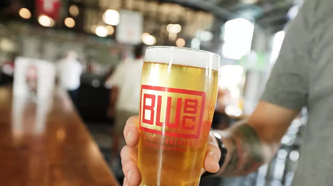 A hand holds out a pint of beer from Brick West Brewing Co.